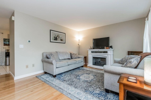 living area with baseboards, light wood-style floors, and a glass covered fireplace