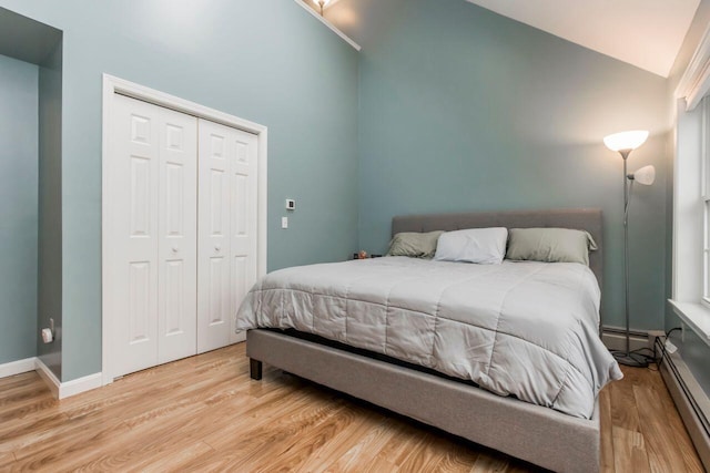 bedroom with a closet, wood finished floors, lofted ceiling, and a baseboard radiator