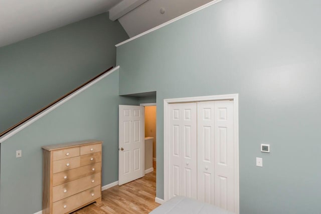 bedroom with light wood finished floors, baseboards, beam ceiling, a closet, and high vaulted ceiling