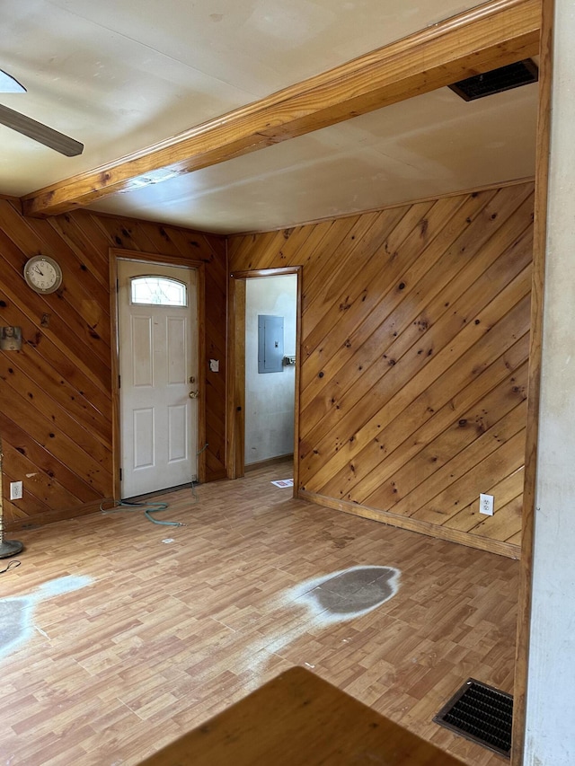 foyer entrance featuring visible vents, ceiling fan, wood walls, light wood-type flooring, and beam ceiling