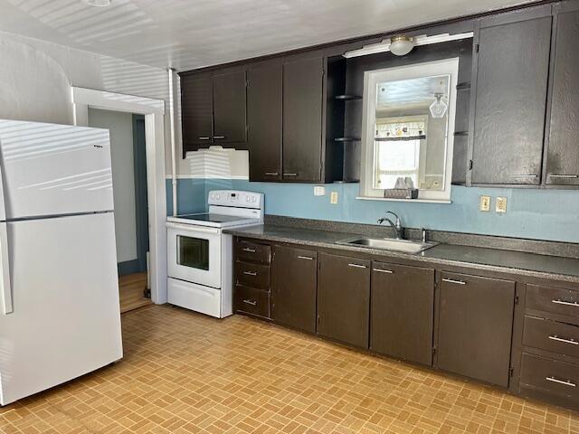 kitchen with dark countertops, dark brown cabinetry, white appliances, and a sink