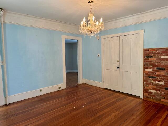 unfurnished room featuring a chandelier, baseboards, wood finished floors, and crown molding