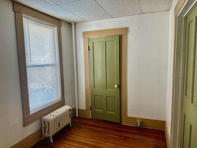 spare room with radiator, dark wood-style flooring, and a drop ceiling