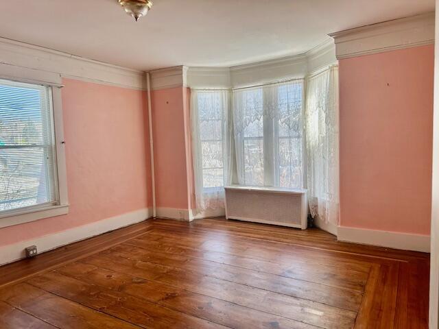 empty room with baseboards, hardwood / wood-style floors, and crown molding