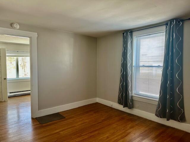 unfurnished room featuring a baseboard heating unit, baseboards, and wood finished floors