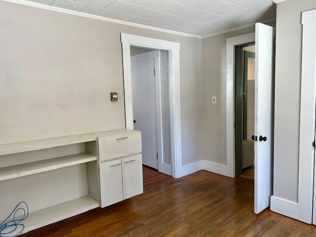 interior space featuring dark wood-style floors, radiator, crown molding, and baseboards