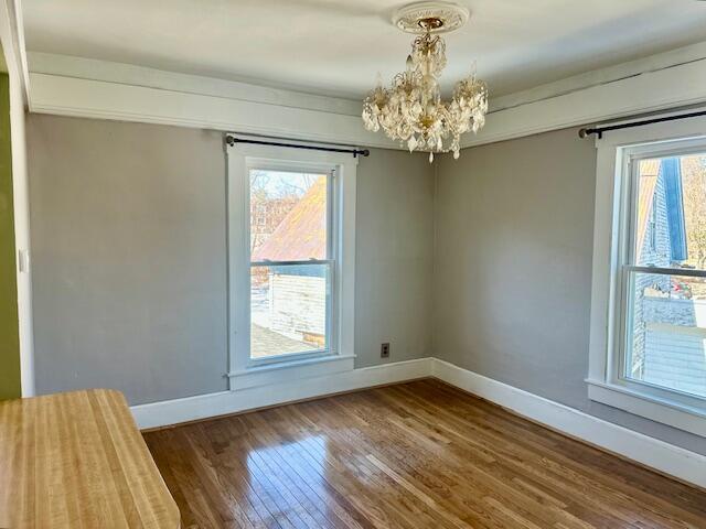 spare room featuring a notable chandelier, wood finished floors, and baseboards