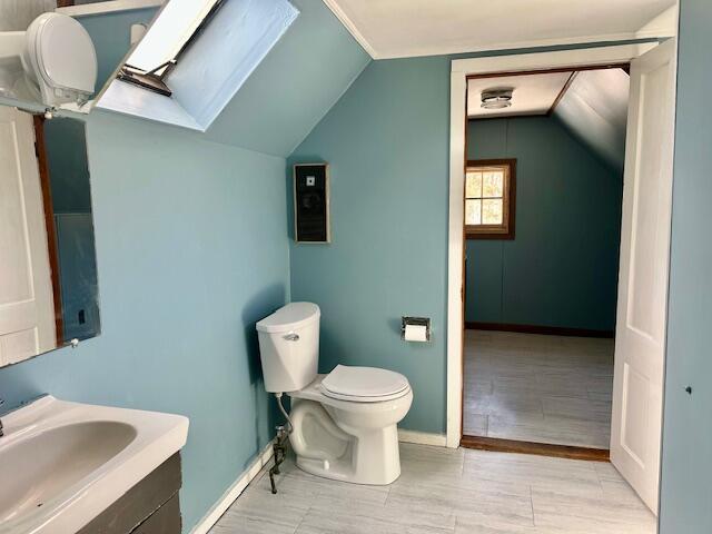 bathroom featuring vanity, lofted ceiling with skylight, toilet, and baseboards