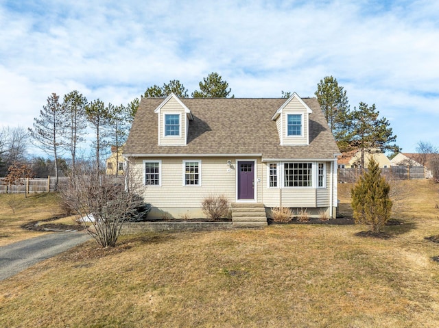 cape cod home featuring entry steps, a shingled roof, a front yard, and fence