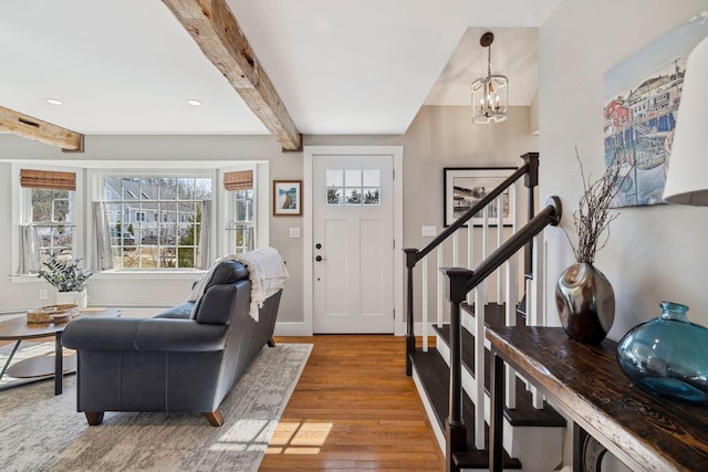 entrance foyer featuring beam ceiling, wood finished floors, stairway, an inviting chandelier, and baseboards