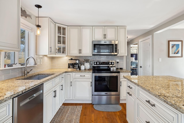 kitchen featuring a sink, backsplash, dark wood finished floors, appliances with stainless steel finishes, and glass insert cabinets