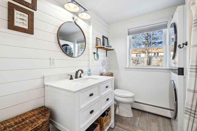 bathroom featuring toilet, wood finished floors, wood walls, a baseboard radiator, and vanity