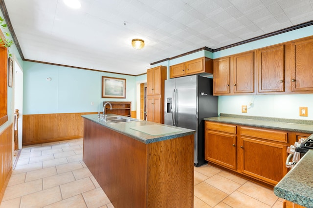 kitchen with a kitchen island with sink, a sink, appliances with stainless steel finishes, wainscoting, and crown molding