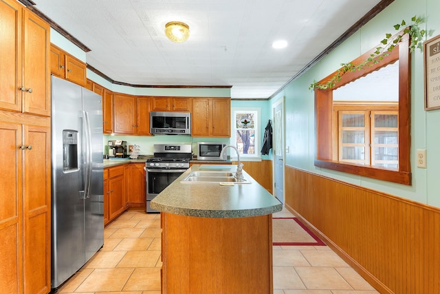 kitchen featuring a sink, crown molding, a wainscoted wall, appliances with stainless steel finishes, and a kitchen island with sink