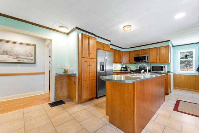 kitchen featuring visible vents, an island with sink, ornamental molding, brown cabinets, and stainless steel appliances