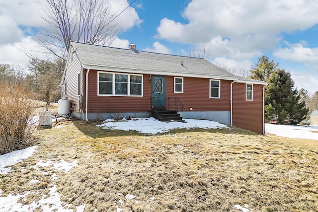 snow covered back of property with roof with shingles and a chimney