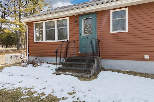 snow covered property entrance with a shingled roof