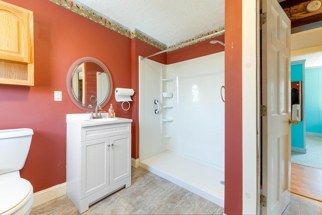 full bathroom with toilet, a textured ceiling, a shower stall, baseboards, and vanity