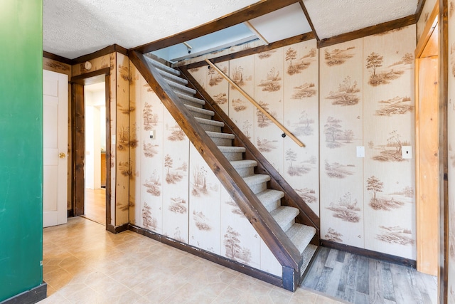 stairway with baseboards, a textured ceiling, wood finished floors, and wallpapered walls