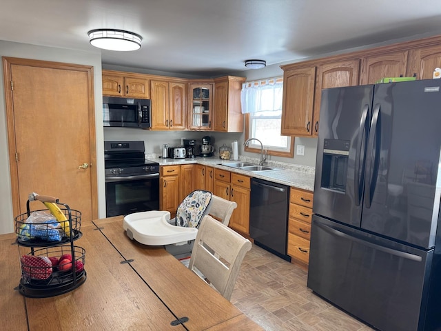 kitchen with a sink, black appliances, light countertops, glass insert cabinets, and brown cabinets