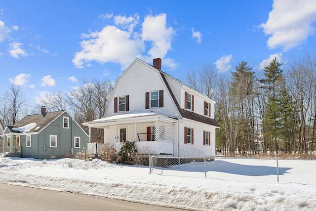 dutch colonial with a fenced front yard, a gambrel roof, a porch, and a chimney