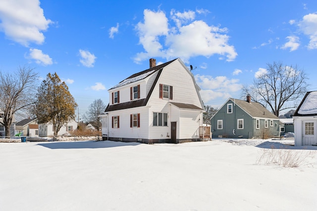 snow covered back of property featuring a gambrel roof and a chimney