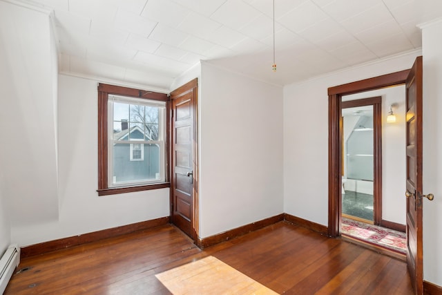 spare room with baseboards, baseboard heating, dark wood finished floors, and crown molding