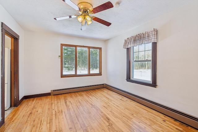 spare room with a baseboard radiator, light wood-style floors, a healthy amount of sunlight, and a textured ceiling