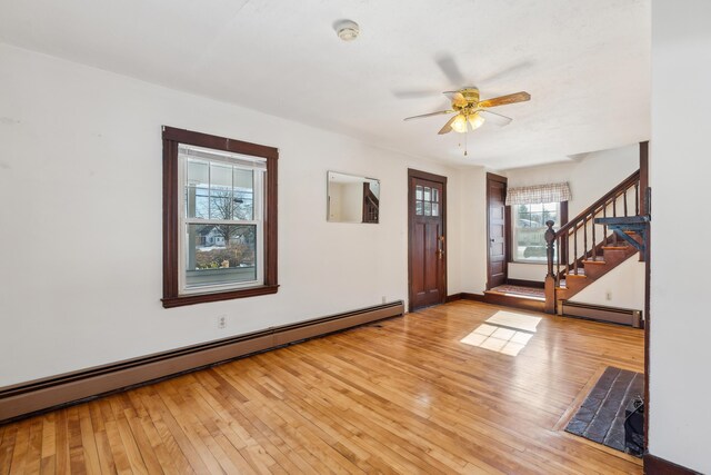 entrance foyer featuring a baseboard heating unit, light wood-style floors, baseboards, ceiling fan, and stairs