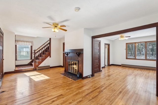 unfurnished living room with light wood-style flooring, a brick fireplace, and a baseboard radiator