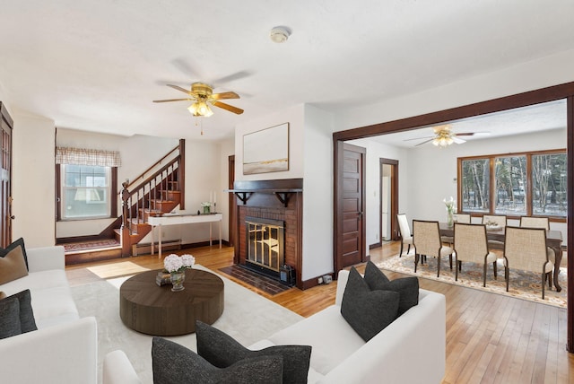 living area featuring a ceiling fan, a fireplace, stairs, light wood-style floors, and baseboard heating