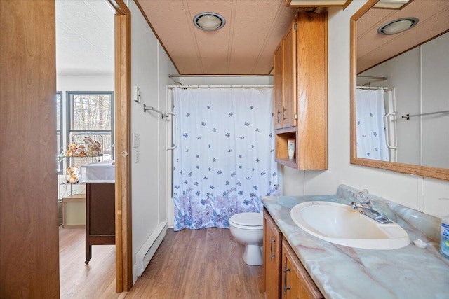 bathroom featuring curtained shower, toilet, wood finished floors, vanity, and a baseboard radiator