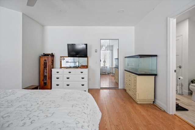 bedroom featuring baseboards, ensuite bath, and light wood finished floors