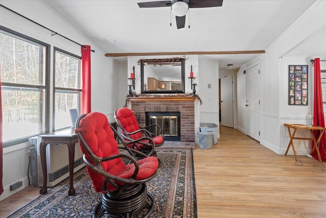 living room with light wood-style flooring, a fireplace, a ceiling fan, and ornamental molding