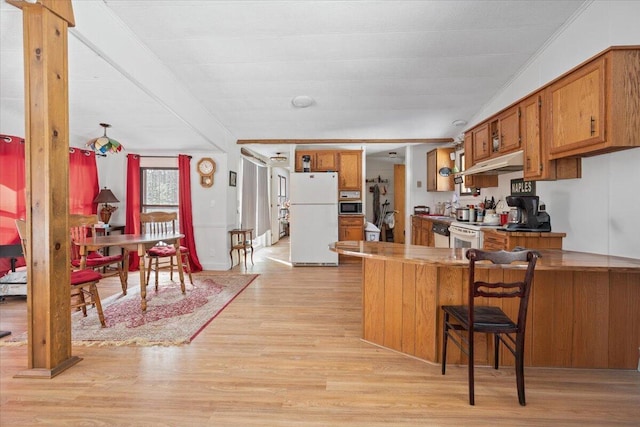 kitchen featuring brown cabinets, light wood-style flooring, under cabinet range hood, white appliances, and a peninsula