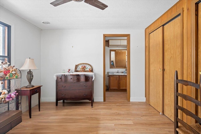 hall with light wood finished floors, a textured ceiling, baseboards, and a sink