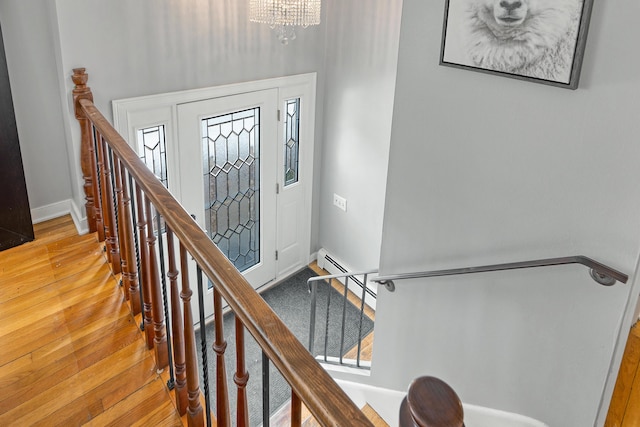 foyer with a baseboard heating unit, baseboards, stairway, light wood-style flooring, and a notable chandelier