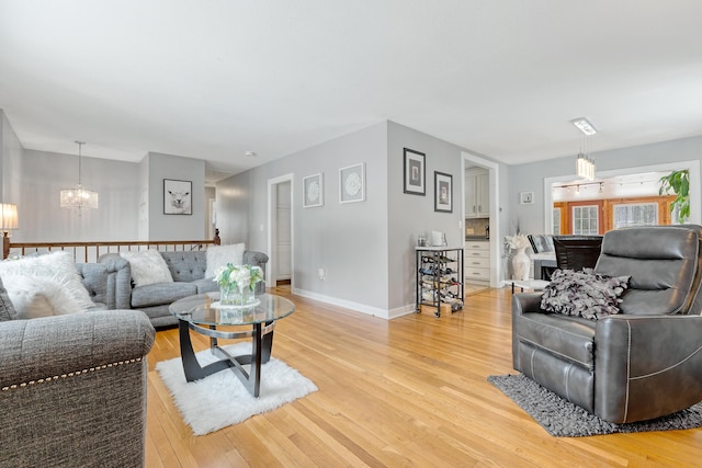 living room featuring baseboards, an inviting chandelier, and light wood-style flooring