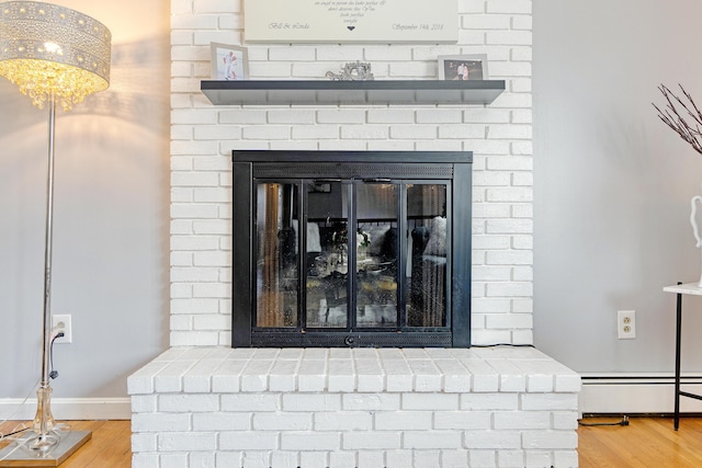 interior details featuring a baseboard radiator, baseboards, a brick fireplace, and wood finished floors