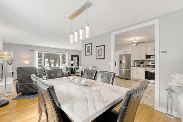 dining area featuring baseboards, light wood-style flooring, and ceiling fan with notable chandelier