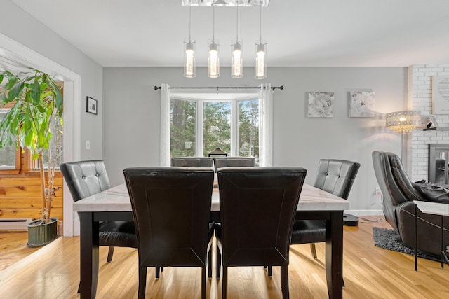 dining area featuring a brick fireplace, light wood-type flooring, and baseboard heating