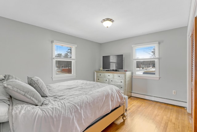 bedroom featuring multiple windows, light wood-type flooring, and a baseboard heating unit