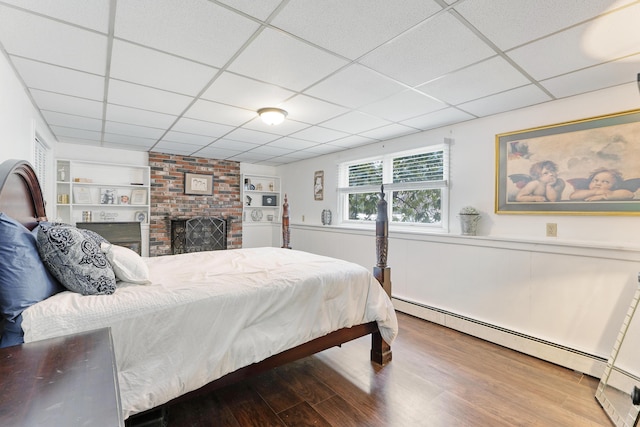 bedroom featuring a fireplace, wood finished floors, a paneled ceiling, and a baseboard radiator