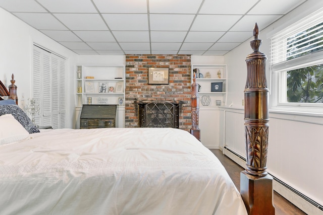 bedroom with a fireplace, a paneled ceiling, wood finished floors, and a baseboard radiator