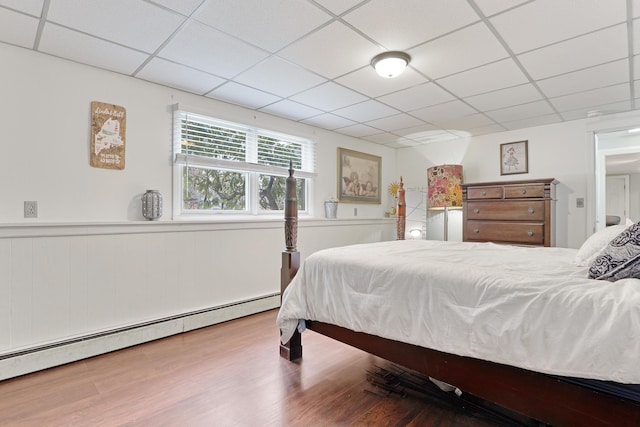 bedroom featuring a baseboard heating unit, a paneled ceiling, wood finished floors, and a wainscoted wall