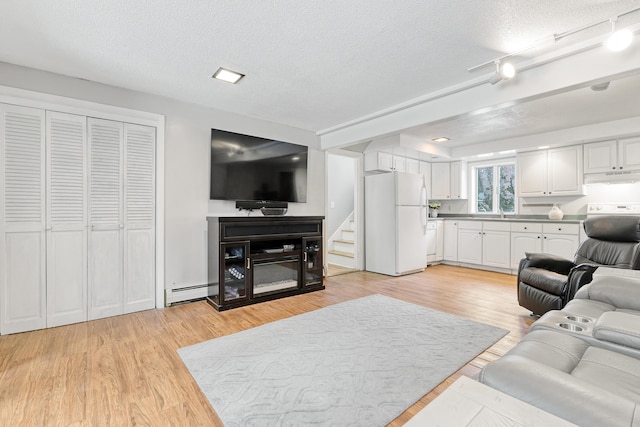 living area featuring stairway, light wood-style floors, baseboard heating, and a textured ceiling