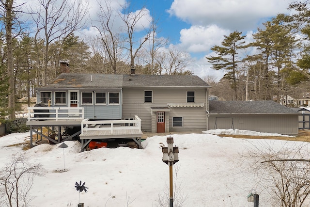 snow covered rear of property featuring a sunroom, roof with shingles, and a wooden deck