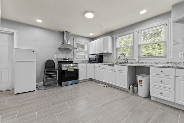 kitchen featuring light stone counters, a sink, white cabinetry, appliances with stainless steel finishes, and wall chimney exhaust hood