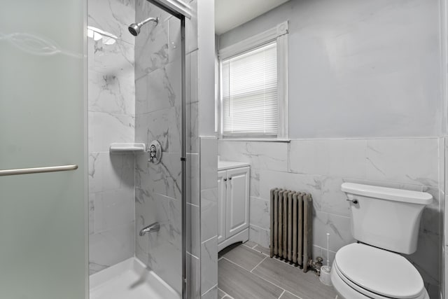 bathroom featuring toilet, radiator heating unit, a marble finish shower, tile walls, and vanity