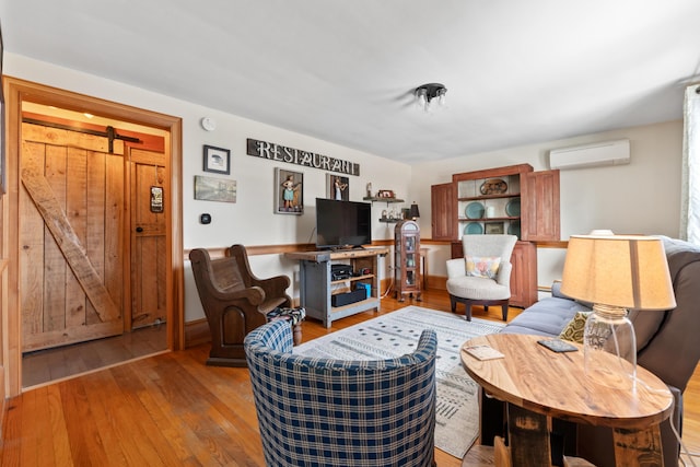 living area featuring a barn door, hardwood / wood-style flooring, and a wall unit AC